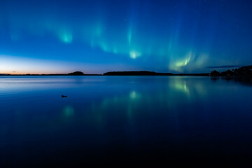 Northern lights dancing over calm lake in Farnebofjarden national park in north of Sweden