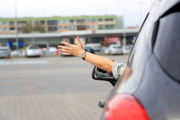 Dłoń kobiety, ręka wysunięta przez okno samochodu osobowego, suwa, na placu przed marketem. - obrazy, fototapety, plakaty