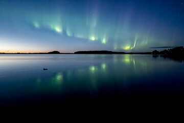 Northern lights dancing over calm lake in Farnebofjarden national park in north of Sweden