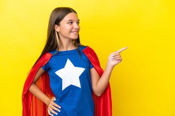 Little caucasian superhero girl isolated on yellow background pointing finger to the side and presenting a product © luismolinero