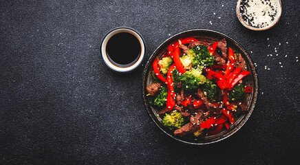 Stir fry vegetables with beef, paprika and broccoli with sesame seeds in bowl on black table  background, top view