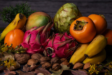 Close-up of tropical autumn fruits, pitahaya or dragon fruit surrounded by bananas, custard apples, persimmons, mango and dried fruits such as almonds and walnuts.
