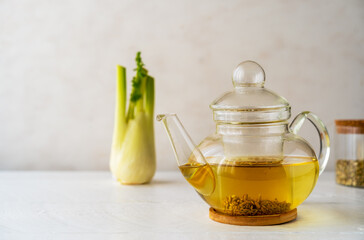 Fennel tea in a glass teapot, fresh fennel bulb, fennel seeds on white wooden table with light...