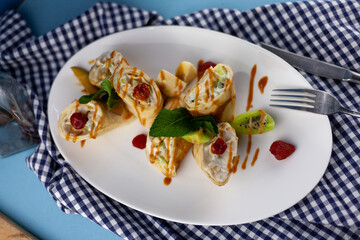 Simple homemade pancakes cut with banana, kiwi, strawberry jam on a white plate. Creamy curd filling. The food is decorated with mint. Rolled thin roll of pancake.