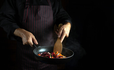 The chef prepares vegetables in a frying pan. Delicious vegetarian food. Advertising space on a black background