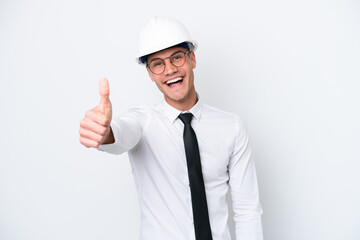 Young architect caucasian man with helmet and holding blueprints isolated on white background with thumbs up because something good has happened