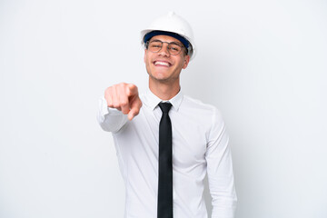 Young architect caucasian man with helmet and holding blueprints isolated on white background pointing front with happy expression