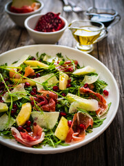 Fresh salad - prosciutto di Parma, pomegranate, pear, leafy vegetables and parmesan on wooden background
