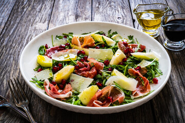 Fresh salad - prosciutto di Parma, pomegranate, pear, leafy vegetables and parmesan on wooden background
