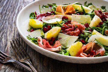 Fresh salad - prosciutto di Parma, pomegranate, pear, leafy vegetables and parmesan on wooden background
