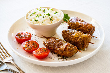 Wrapped pork served with white rice and cherry tomatoes on white table
