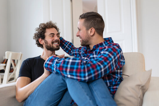 Cheerful young gay couple sitting together. Two affectionate male lovers smiling cheerfully while embracing each other. Young gay coupe being romantic.