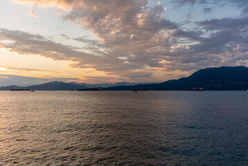 Sunset on the sea in front of Vancouver with container ships, sail boat and stand-up paddles