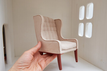 Armchair for a doll in a hand near a doll house. Miniature and roombox hobby.