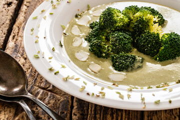 Cream broccoli soup with almonds and oregano on wooden table
