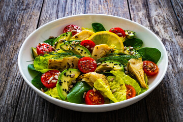 Fresh vegetable salad - avocado, artichoke, lettuce, cherry tomatoes, cucumber, arugula and spinach on wooden table 