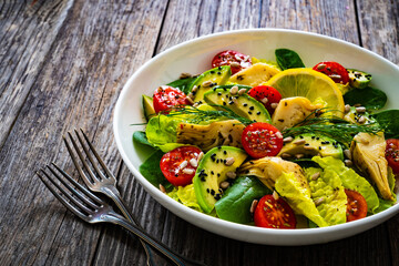 Fresh vegetable salad - avocado, artichoke, lettuce, cherry tomatoes, cucumber, arugula and spinach on wooden table 