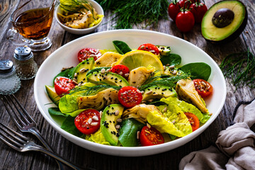 Fresh vegetable salad - avocado, artichoke, lettuce, cherry tomatoes, cucumber, arugula and spinach on wooden table 