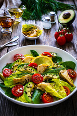Fresh vegetable salad - avocado, artichoke, lettuce, cherry tomatoes, cucumber, arugula and spinach on wooden table 