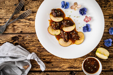 Pork cheeks in sauce with apple on wooden table