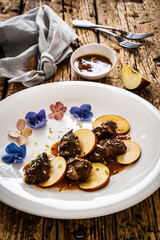 Pork cheeks in sauce with apple on wooden table
