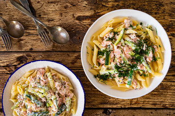 Penne with roasted salmon nuggets, dill and zucchini in cream sauce on wooden table
