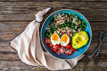 Boiled eggs with avocado, boiled red and white rice, cherry tomatoes, spinach and parmesan on wooden table
