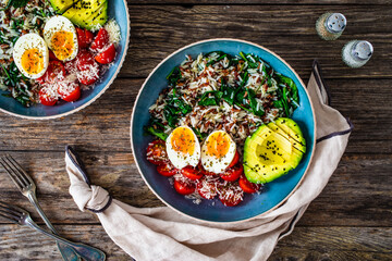 Boiled eggs with avocado, boiled red and white rice, cherry tomatoes, spinach and parmesan on wooden table
