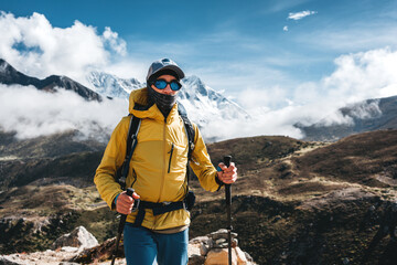 Solo outdoor traveler walk across huge mountains massif wearing yellow jacket and travel backpack. Adventure tourist going along mountain landscape