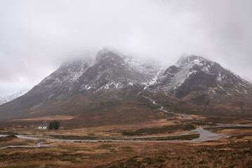 Dramatic Winter landscape image of white cottage at foot of Stob Dearg Buachaille Etive Mor peak in Scottish Highlands