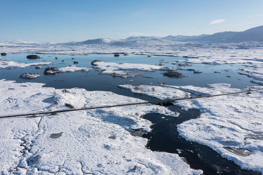 Beautiful aerial drone Winter landscape images of Loch Ba and snow covered mountains in background in Scottish Highlands on blue sky Winter day