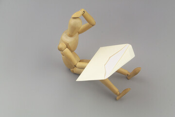 Thinking wooden figurine holding envelope with white letter on gray background. News concept.