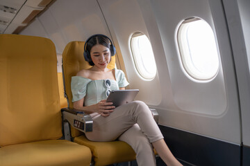 Joyful asian woman sits in the airplane and using tablet while go to travel