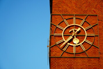 Golden clock on a brick building with a blue sky on the left