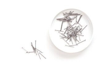 Small thin metal nails, hardware, lying in a round container.