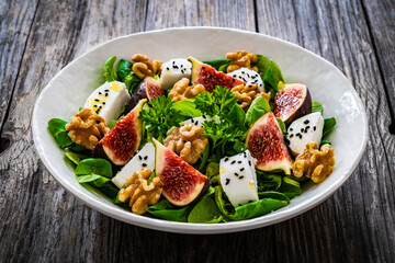 Fresh salad - goat cheese, fig, walnuts and leafy greens on wooden table
