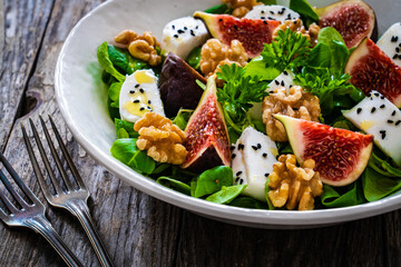 Fresh salad - goat cheese, fig, walnuts and leafy greens on wooden table
