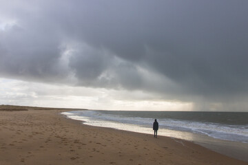 silhouette d'un jeune homme sur la plage sous un ciel orageux