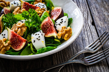 Fresh salad - goat cheese, fig, walnuts and leafy greens on wooden table
