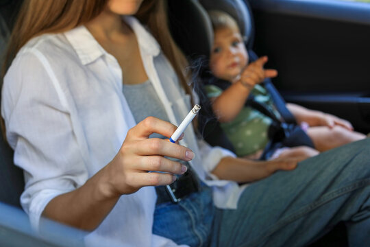 Mother with cigarette and child in car, closeup. Don't smoke near kids