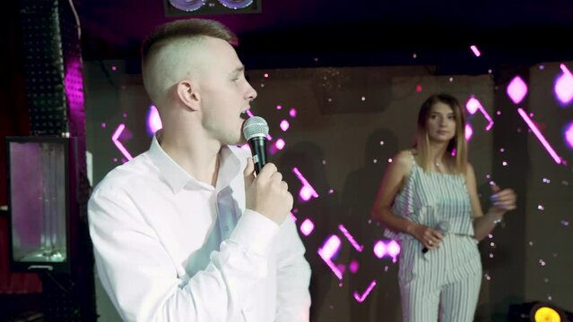 Young Caucasian female and male singing in the stage with colorful light in bckg