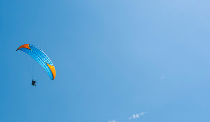 Against of blue summer cloudy sky, paraglider athlete flies on blue-yellow ultralight aircraft - paraglider. Extreme sport and recreation.