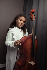 Beautiful girl in a stylish dress stands with a cello.