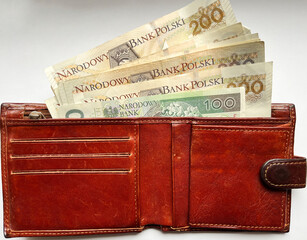 Brown leather wallet with 200 and 100 zloty bills in close-up on a white isolated background. Payment in zloty in Poland