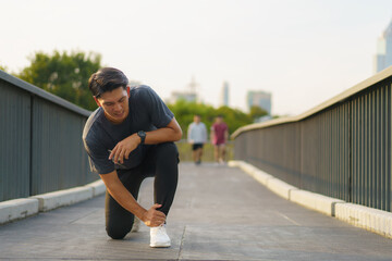 Asian Runner suffering ankle injury after sport outdoors in a city outskirts park
