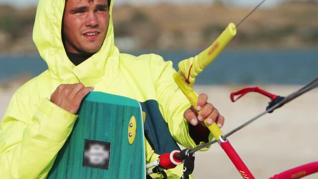 Wet kiteboarder standing with a kite bar by the shore sea bay. Freestyle kiter looking at camera after kiteboarding training session on pond spot. Extreme water sports. Slow motion 120 fps.