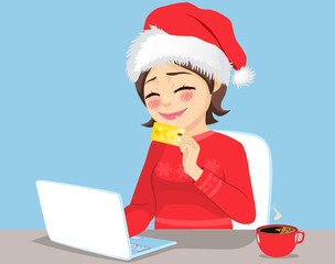 Smiling woman excited doing online Christmas shopping sitting wearing red Santa hat holding her golden credit card to use on her laptop computer. X-mas gift list concept