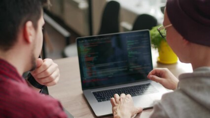 Two hipster coworkers sharing ideas about project sitting with laptops in spacious open space office. Developers discuss application program code. Coder and manager consulting software architecture.