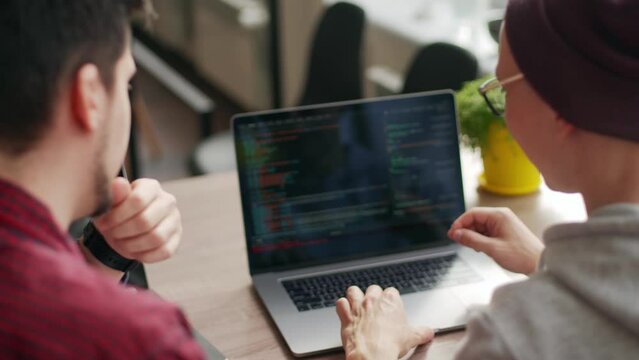 Two hipster coworkers sharing ideas about project sitting with laptops in spacious open space office. Developers discuss application program code. Coder and manager consulting software architecture.
