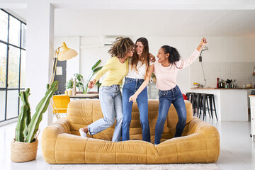 Three funny female friends dancing and singing on the sofa at home. Multiracial happy women play and celebrate the joy of life Cheerful girls enjoy together at home having fun. . High quality photo